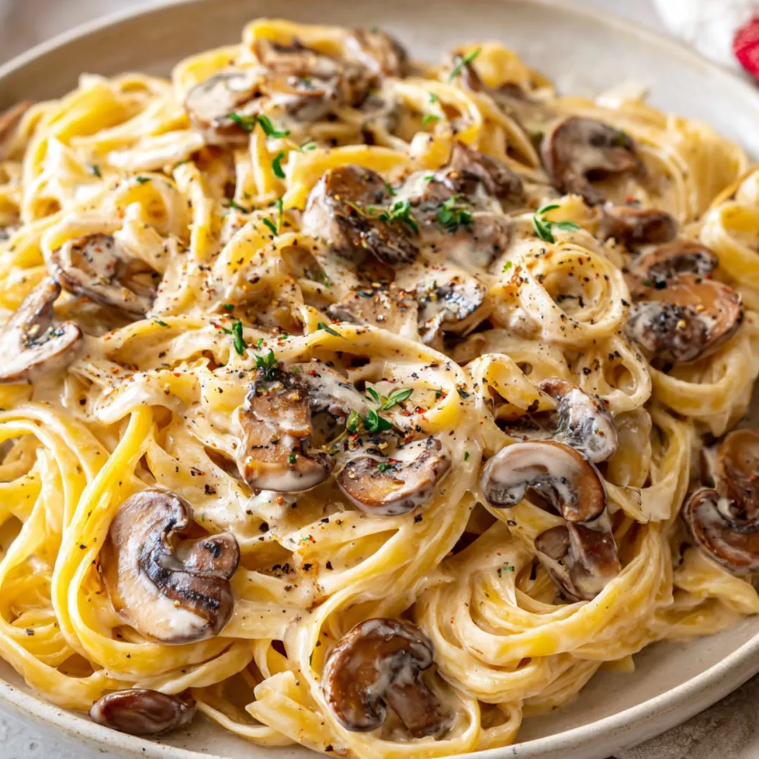Pasta on a plate covered with mushrooms and parmesan cheese.
