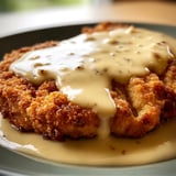 Chicken Fried Steak on a plate all drenched in rich Gravy.