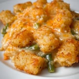 A plate packed with cheesy green beans and golden tater tots.