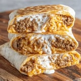 Some burritos stacked on a wood table.