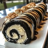 Slices of a chocolate cake roll packed with Oreo filling and topped with white chocolate, served on a plate.