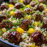 Bowl of rice topped with meatballs and colorful veggies.