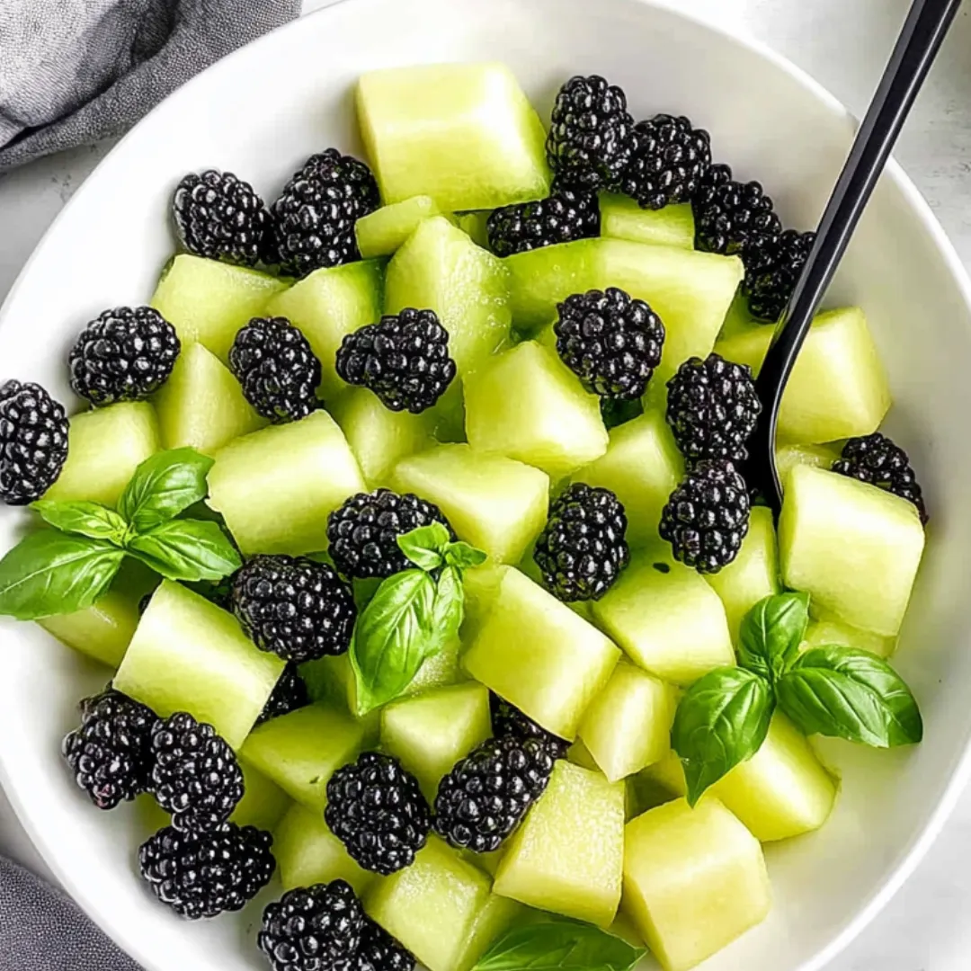 A bowl of fruit with blackberries, green apples, and mint.