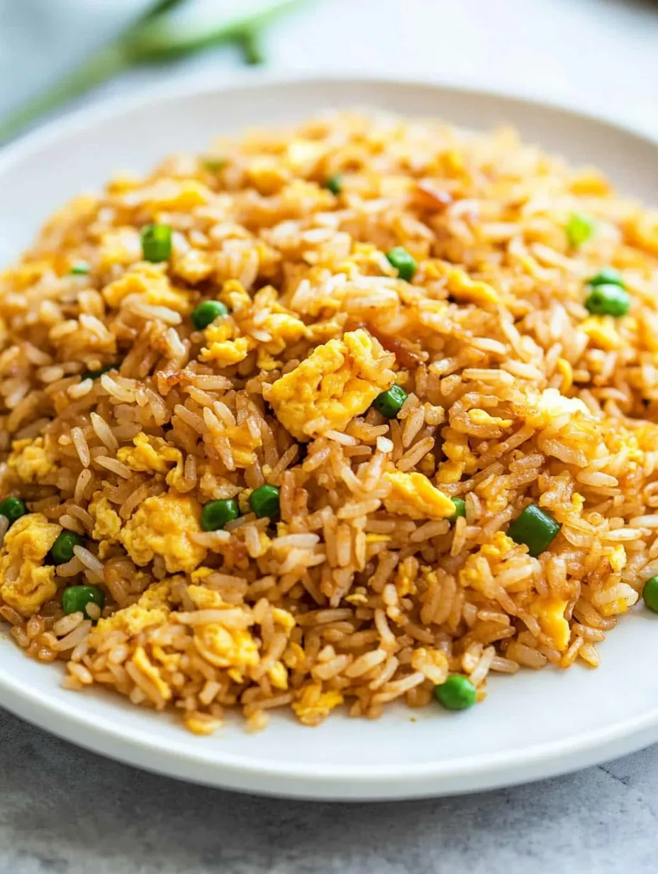 A bowl of fried rice with chunks of egg and green peas.