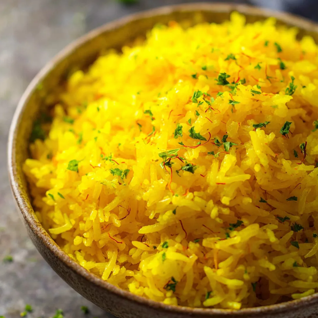 Yellow rice in a bowl topped with fresh green herbs.