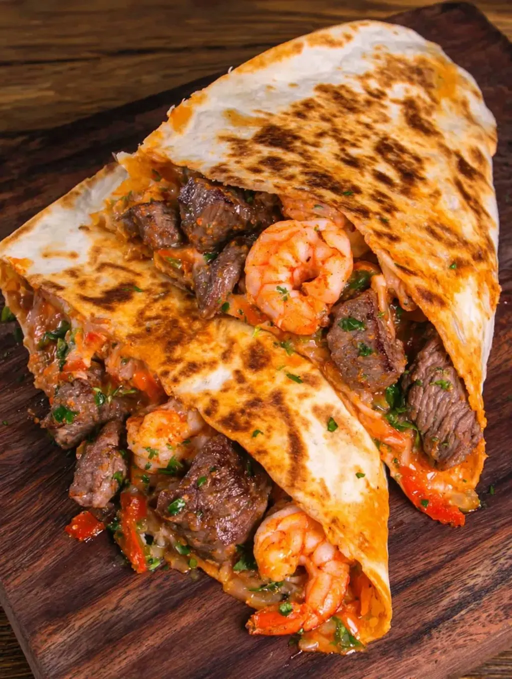 A burrito stuffed with shrimp and steak resting on a wood table.