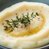A bowl of mashed potatoes with herbs on top.
