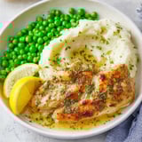 A bowl of food with chicken, potatoes, and peas.