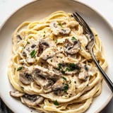 Pasta topped with mushrooms and fresh herbs on a plate.