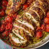 Sizzling chicken and tomatoes in a pan with fresh herbs.