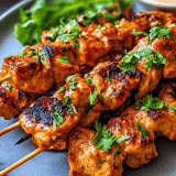 Grilled chicken skewers piled up on a plate.