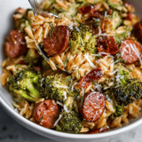 Pasta piled in a bowl with slices of sausage and broccoli peeking through.