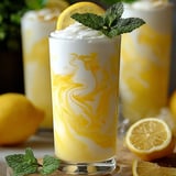 Bright yellow lemonade poured in a glass with a lemon wedge on top.