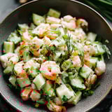 Shrimp and cucumber salad in a bowl with fresh herbs on top.