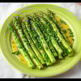 Bright green asparagus set on a plate, topped with citrusy sauce.