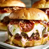 Two cheesy pepperoni burgers on a plate.