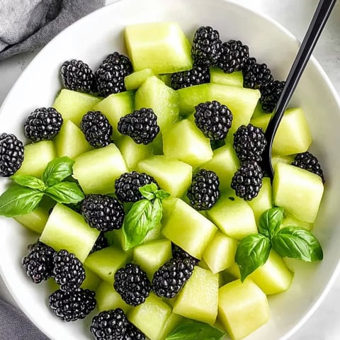 A bowl of fruit with blackberries, green apples, and mint.